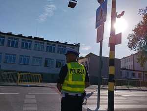 obraz przedstawia policjanta sprawdzającego oznakowania przejść dla pieszych przy szkole