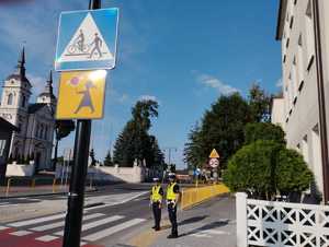 obraz przedstawia policjantów sprawdzających oznakowania przejść dla pieszych przy szkole