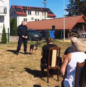 obraz przedstawia policjanta z psem na spotkaniu z seniorami