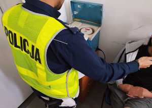 obraz przedstawia policjanta obsługującego urządzenie do badania stanu trzeźwości