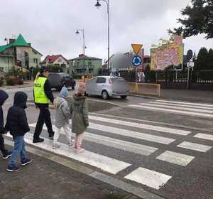 obraz przedstawia policjantkę z dziećmi przechodzącymi przez przejście dla pieszych