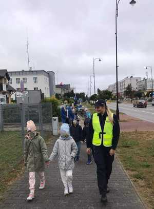 obraz przedstawia policjantkę z dziećmi przechodzącymi przez przejście dla pieszych
