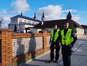 obraz przedstawia policjantów patrzących na cmentarz, w tle kościół