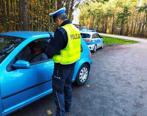 obraz przedstawia policjanta stojącego przy pojeździe