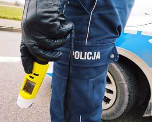 obraz przedstawia policjanta trzymającego urządzenie do pomiaru trzeźwości