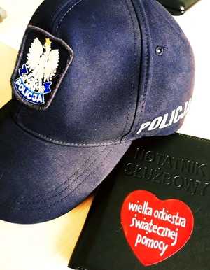 obraz przedstawia czapkę policjanta wraz z notatnikiem, na którym widnieje naklejka  31. Finału Wielkiej Orkiestry Świątecznej Pomocy