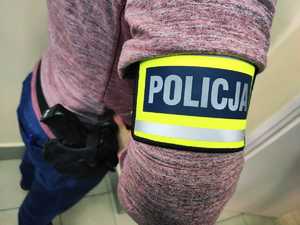 obraz przedstawia ramię policjanta z opaską z napisem policja