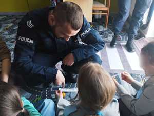 obraz przedstawia policjanta rozmawiającego z dziećmi