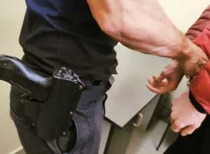 obraz przedstawia policjanta zakładającego kajdanki zatrzymanemu