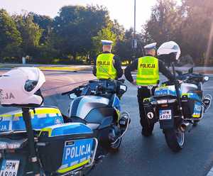 obraz przedstawia policjantów patrzących na drogę, w tle motocykle