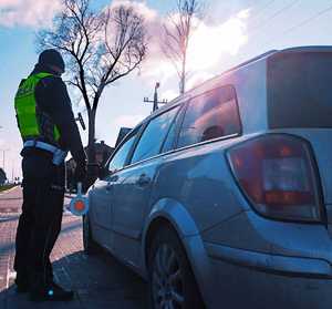 obraz przedstawia policjanta stojącego przy pojeździe