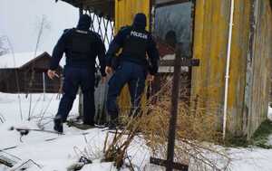 obraz przedstawia policjantów na tle drewnianego budynku