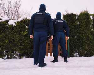 obraz przedstawia policjantów na tle drewnianego budynku