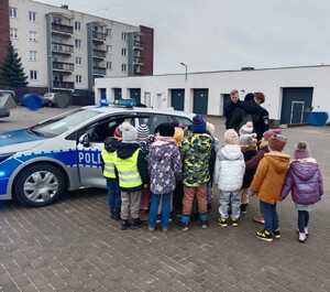 obraz przedstawia policjantkę z dziećmi na tle radiowozu