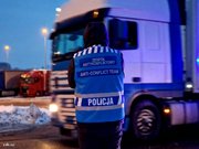 obraz przedstawia mężczyznę w niebieskiej kamizelce z napisem policja na tle pojazdu ciężarowego