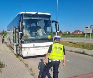 obraz przedstawia policjanta kontrolującego autokar